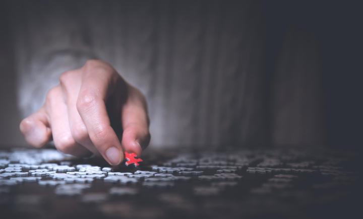 man holding red puzzle piece around gray puzzle pieces