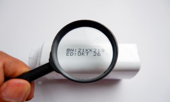 A hand holding a magnifying glass over a label-printed expiration date on a plastic package