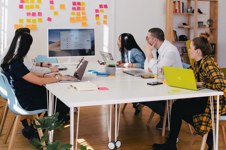 5 people sitting around a table, all looking at a computer monitor