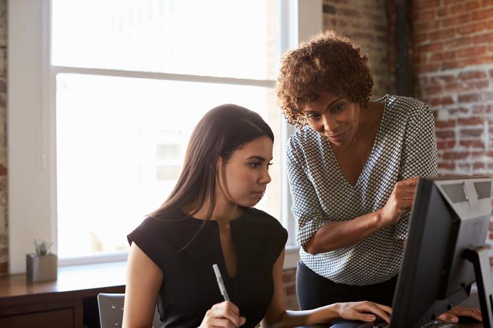 Woman mentoring coworker in front of computer screen