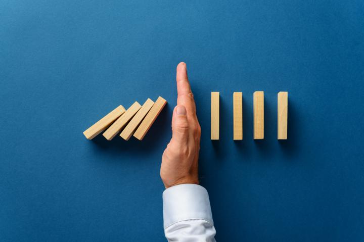 Photo of hand stopping the tumbling of dominoes; example of business crisis management recovery