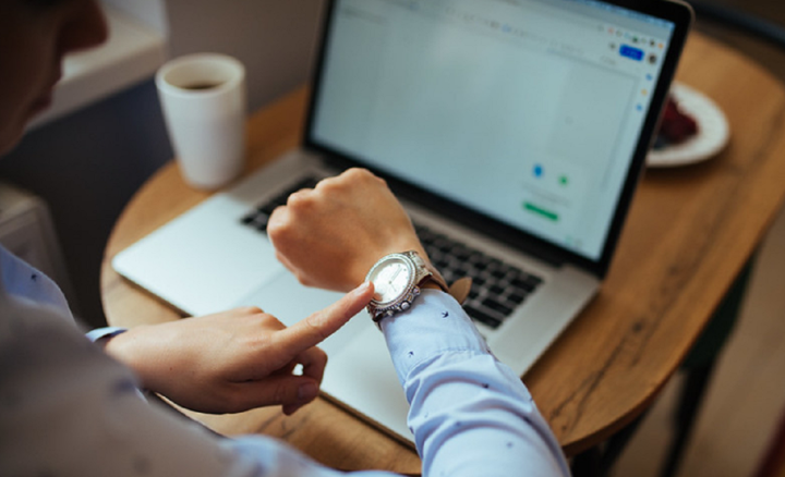 A man looks at his watch while reviewing marketing metrics on a laptop