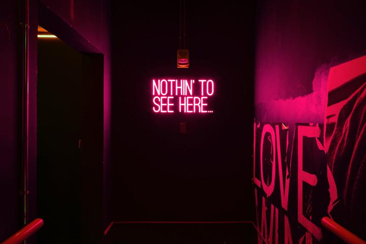Neon sign that says "Nothin to see here" that is glowing in a dark room
