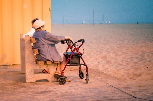 Woman with assistive walker sits on boardwalk. Unable to access the water she gazes at the ocean from afar