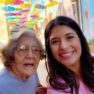 Caregiver taking a smiling selfie with her grandmother and colourful umbrellas in the background