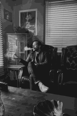 Copywriter Michael de la Guerra sitting in a cigar lounge blowing smoke rings.